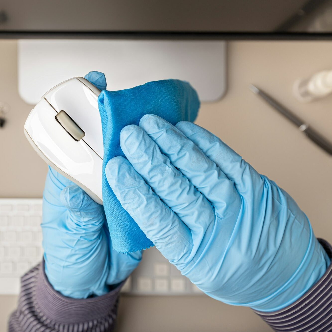 Gloved hand disinfecting a computer mouse